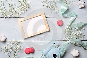 Modern polaroid camera, macaroon cookies, photo frame, flowers on rustic blue wooden background. Top view, tender minimal flat lay