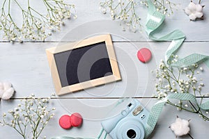 Modern polaroid camera, macaroon cookies, photo frame, flowers on rustic blue wooden background. Top view, tender minimal flat lay