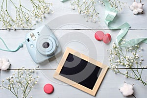 Modern polaroid camera, macaroon cookies, photo frame, flowers on rustic blue wooden background. Top view, tender minimal flat lay