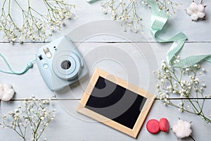 Modern polaroid camera, macaroon cookies, photo frame, flowers on rustic blue wooden background. Top view, tender minimal flat lay