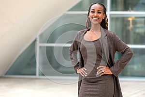 Modern portrait of African American female business person standing by office building, architecture firm, law, finance or other p