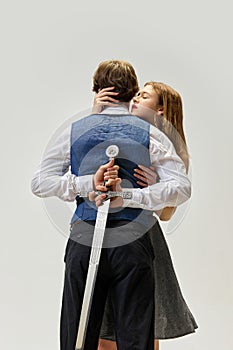 Modern portrait of young couple in codependent hypertrophied toxic relationship. Woman hugs man with sword behind his