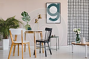 Modern poster on pastel pink wall of elegant living room interior with round wooden table with chairs