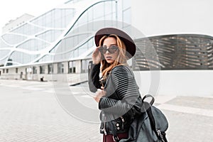 Modern pretty stylish hipster young woman in a fashionable hat in vintage dark sunglasses in a black jacket