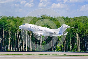 A modern private white business jet takes off against the backdrop of a forest. Jet business aviation. Travel or