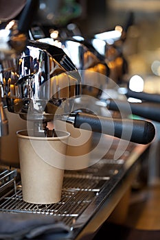 Modern professional espresso machine with coffee pouring into take away paper cup