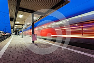 Modern railway station with high speed passenger train on railroad track in motion at night