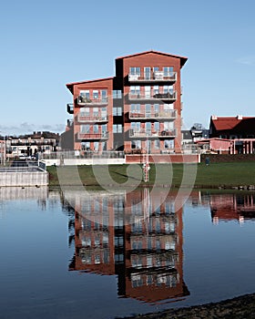 A modern red brick apartment building reflecting in the nearby lake in Lund Sweden