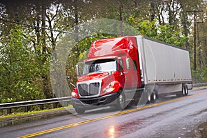 Modern red glossy in rain semi truck trailer on raining road