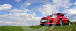 Modern red luxury car on the grass under the cloudy sky