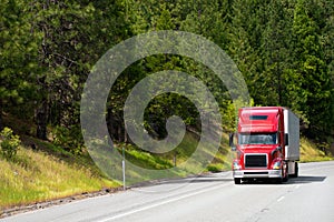 Modern red semi truck with dry van trailer driving on road with