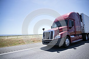 Modern red semi truck and reefer trailer on road in sunny day photo