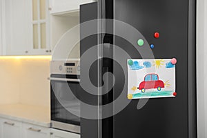 Refrigerator with child`s drawing and magnets in kitchen photo