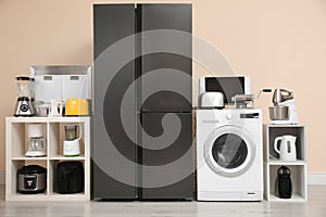 Modern refrigerator and household appliances near beige wall indoors