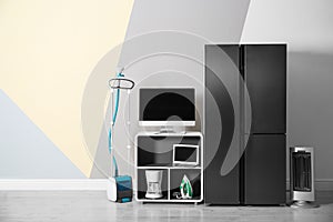 Modern refrigerator and other household appliances near color wall