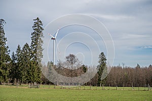 Modern renewable energy wind turbine at the horizon with meadow and forest in front