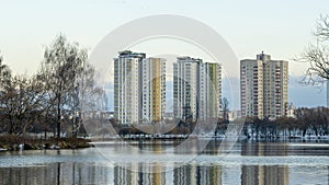 Modern residential area in city near lake with the first snow. Tall residential buildings are visible behind the trees