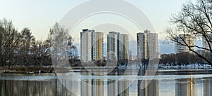 Modern residential area in city near lake with the first snow. Tall residential buildings are visible behind the trees