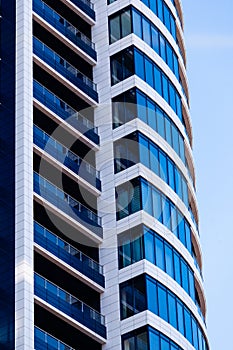 The modern residential building is dark blue with white stripes and large glass windows against the sky. Skyscraper close up.