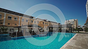 Modern residential complex with large pool, patio area, sunny skies in urban environment, showcasing comfortable living