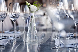 Modern restaurant setting, glass vase with bouquet flowers on table in restaurant. Wine and water glasses stand on wooden table.