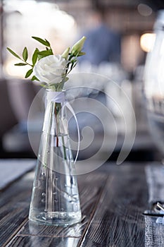 Modern restaurant setting, glass vase with bouquet flowers on table in restaurant. Wine and water glasses stand on wooden table.
