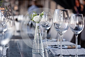 Modern restaurant setting, glass vase with bouquet flowers on table in restaurant. Wine and water glasses stand on wooden table.