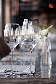 Modern restaurant setting, glass vase with bouquet flowers on table in restaurant. Wine and water glasses stand on wooden table.