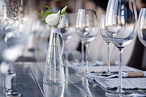 Modern restaurant setting, glass vase with bouquet flowers on table in restaurant. Wine and water glasses stand on wooden table.