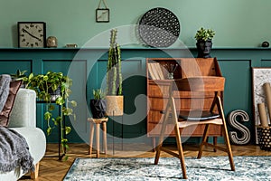 Modern and retro composition of home office interior with wooden cabinet, chair, plants, decoration.