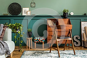 Modern and retro composition of home office interior with wooden cabinet, chair, plants, decoration.