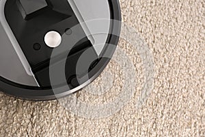 Modern robotic vacuum cleaner on beige carpet. Space for text