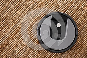 Modern robotic vacuum cleaner on brown rug. Space for text