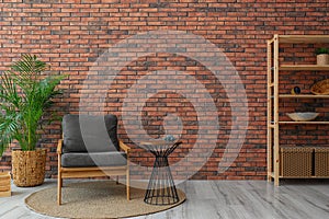 Modern room interior with stylish grey  and potted plant near brick wall