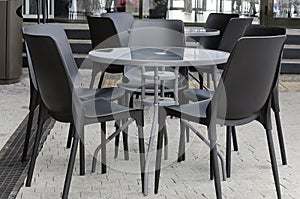 Modern round table and plastic black chairs in a street cafe, close-up