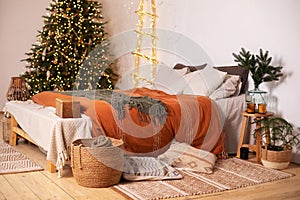 Modern rustic room decoration for new year with decorated Christmas tree, comfortable bed and vase with branches pine fir. Hygge X