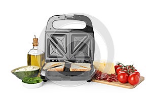 Modern sandwich maker with bread slices and different products on white background