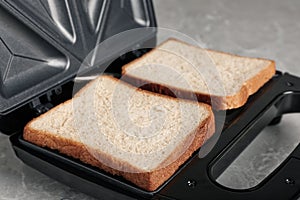 Modern sandwich maker with bread slices on grey table, closeup