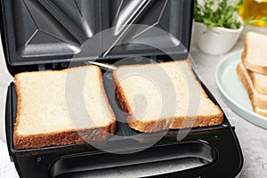 Modern sandwich maker with bread slices on light grey table, closeup