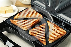 Modern sandwich maker with bread slices on white table, closeup