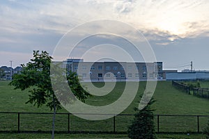 Modern school building - against a backdrop of a cloudy sky at dusk - surrounded by a well-maintained green lawn - bordered by a