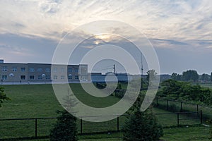 Modern school building - against a backdrop of a cloudy sky at dusk - surrounded by a well-maintained green lawn - bordered by a