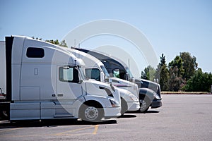 Modern semi trucks stand in row on truck stop parking space