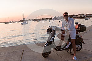 A modern senior businessman in casual clothes sitting on a scooter by the sea and enjoys the sunrise. Selective focus