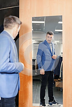 Modern senior in a suit in jeans and sneakers near the mirror. man trying on clothes in a boutique