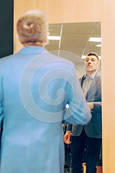 Modern senior in a suit in jeans and sneakers near the mirror. man trying on clothes in a boutique