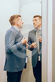 Modern senior in a suit in jeans and sneakers near the mirror. man trying on clothes in a boutique