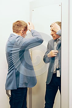 Modern senior in a suit in jeans and sneakers near the mirror. man trying on clothes in a boutique