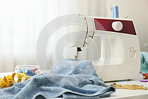 Modern sewing machine, fabric and accessories on table indoors