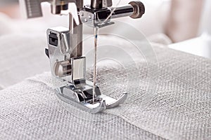 Modern sewing machine presser foot with linen fabric and thread, closeup